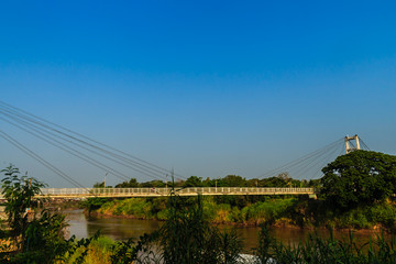 Suspension bridge spanning across Nan river to Phichit railway station in Muang district of Phichit province with blue sky and sunshine. Phichit is a province of Thailand and far 330 km from Bangkok.