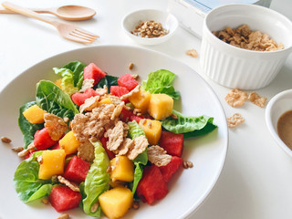 Colorful summer salad with green cos lettuce, mango, watermelon, cereal and sunflower seed on a kitchen table, close up