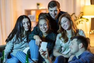 friendship, people, technology and entertainment concept - happy friends with smartphone and drinks watching tv at home in evening