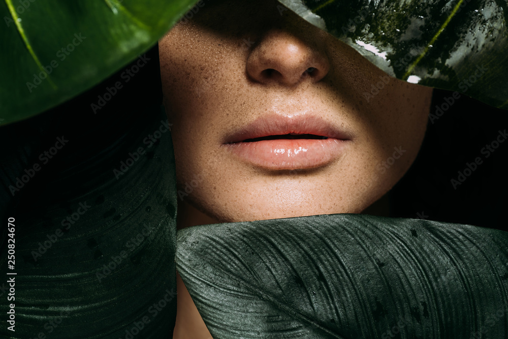 Wall mural cropped view of girl with freckles posing with green tropical leaves