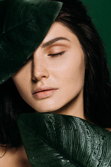 beautiful tender woman with closed eyes and freckles posing with palm leaves