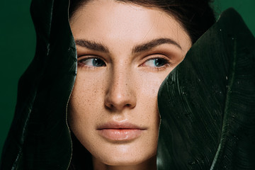 young woman with freckles on face posing with leaves isolated on green