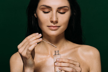 attractive naked woman holding bottle with moisturizing serum isolated on green