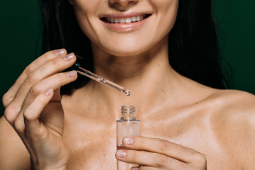 cropped view of smiling naked woman holding pipette and bottle with serum isolated on green
