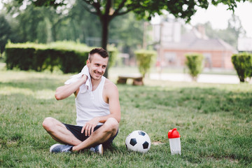 Smiling young man wiping neck while sitting on soccer field at park © Black Ivy Images