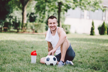 Smiling young man wiping neck while sitting on soccer field at park