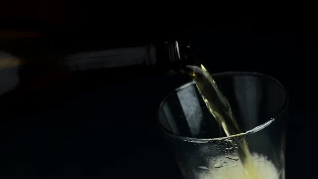 Pouring craft beer from the bottle into drinking glass on dark background close up. 59.9 fps full hd video
