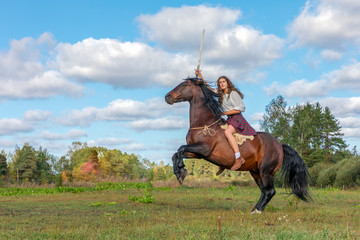 Girl in a Scottish kilt holding a sword in her hand astride horse, who costs on hinder legs