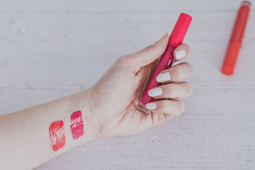 woman's hand holding lipgloss product and testing it surrounded by other make-up items on desk