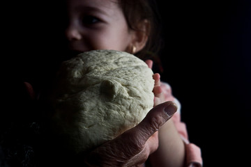 A happy child is watching the dough from which the grandmother makes bread