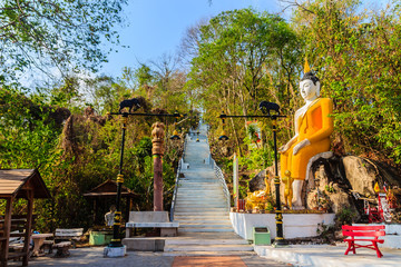 Yellow big Buddha on the stair way to the hill at Wat Khao Rup Chang or Temple of the Elephant Hill, one of the most famous attractions in Phichit province, Thailand. © kampwit