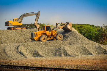 Yellow wheel loader and excavator are working in quarry against the background of crushed stone...