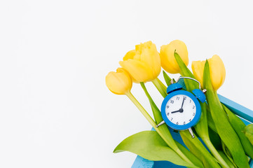 Womans holiday yellow Spring tulips with an alarm clock and blue wooden cart box isolated on white background.Several objects Top horizontal view copyspace