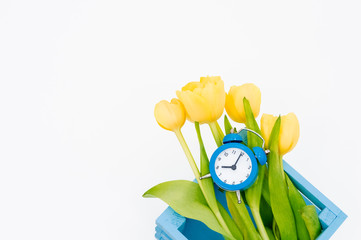 Womans holiday yellow Spring tulips with an alarm clock and blue wooden cart box isolated on white...