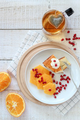 Breakfast flat lay composition with a piece of cake, some slices of orange and  a cup tea with a heart shape tea bag in it
