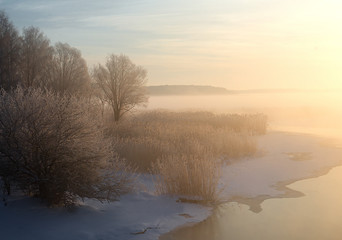 Obraz na płótnie Canvas wonderful winter scene. Frosty, misty morning on the small river. frost covered trees in the warm glow of sunrise on the beach. The beauty of the world