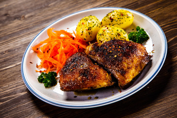 Grilled thighs with boiled potatoes and vegetable salad on wooden table