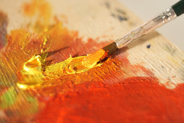 On a wooden palette, brush smears oil paint yellow and orange. The palette is brightly illuminated...