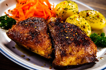 Grilled thighs with boiled potatoes and vegetable salad on wooden table