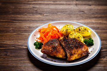 Grilled thighs with boiled potatoes and vegetable salad on wooden table