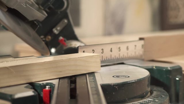 A front view of a miter saw cutting a work piece at a selected angle with sawdust flying. A hand is taking cut work piece