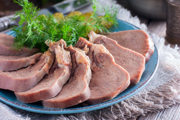 Chopped boiled beef tongue on a plate with fresh herbs and pickled cucumbers, horizontal