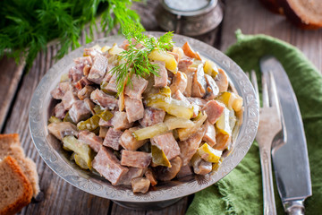 Salad with beef tongue, pickled cucumbers and champignons on a wooden table, horizontal