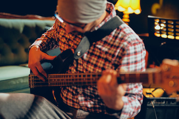 Close up of young man playing bass guitar. Home studio interior.