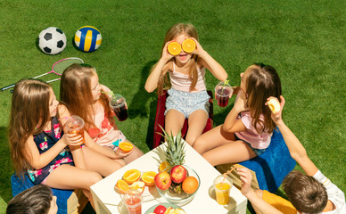 Kids fashion concept. The group of teen boys and girls sitting on green grass at park. Children colorful clothes, lifestyle, trendy colors concepts.