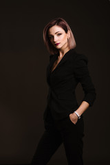 Successful business woman in strict black suit posing in studio