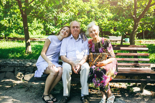 Beautiful old couple is sitting on the bench in the park with their granddaughter. Grandma and grandpa are hugging and smiling. Real love and family relationship photo. Generations concept.