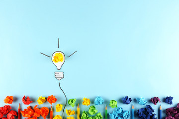 Many different rainbow colored crumpled paper balls on blue gradient background with glowing light bulb as a metaphor for creative idea. Creativity concept. Close up, copy space, top view, flat lay.