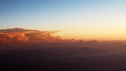 Beautiful sunset cloudscape view from airplane window. Flying over moving pale orange clouds in the evening sunshine. Traveling by air through colorful twilight skyscape with late sun rays.