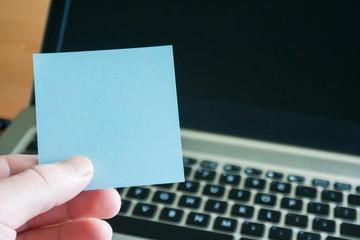 Empty sticky note on laptop keyboard background. Sticky blank in human hand.