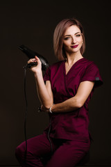 A woman hairdresser posing with hairdryer in studio on the black background
