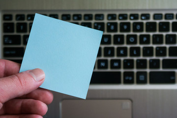 Empty sticky note on laptop keyboard background. Sticky blank in human hand.