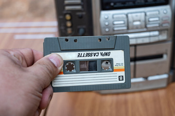 Man hand putting cassette into old fashioned audio tape player on top desk wood background