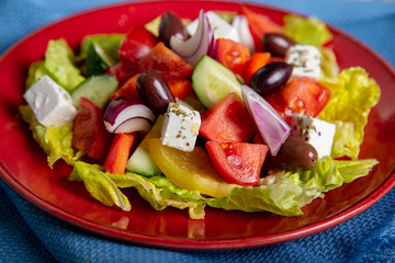 Greek salad of fresh cucumber, tomato, sweet pepper, lettuce, red onion, feta cheese and olives with olive oil on wooden background. Healthy food