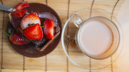 Ice cream cake makeup with strawberry sauce and fresh strawberries set with hot cocoa.
