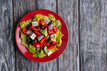 Greek salad of fresh cucumber, tomato, sweet pepper, lettuce, red onion, feta cheese and olives with olive oil on wooden background. Healthy food