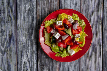 Greek salad of fresh cucumber, tomato, sweet pepper, lettuce, red onion, feta cheese and olives with olive oil on wooden background. Healthy food