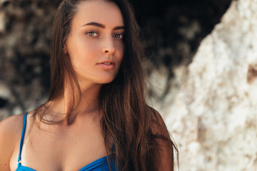 Naklejka premium Sexy brunette girl in blue swimsuit sunbathes on the white sand beach near the rock.