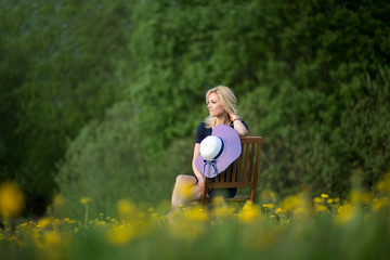 beautiful blonde woman is sitting on a wooden chair with blooming dandelion