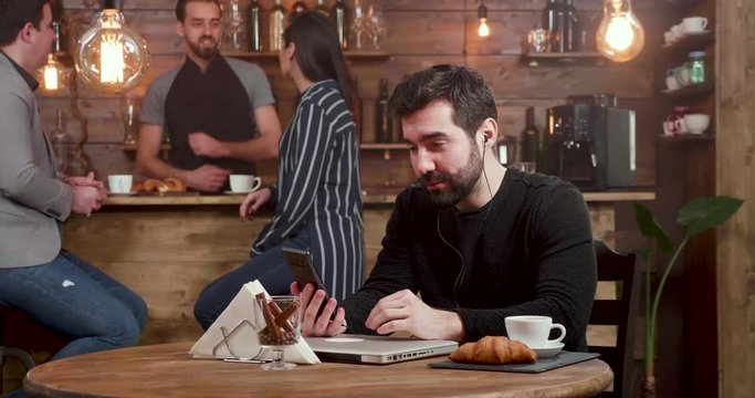 Young handsome man engaged in a video call while serving his coffee in a cafe. Having a friendly video chat while freelancing in a coffee shop.