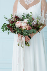 Wedding bouquet with powder-pink peonies and roses in the hands of the bride