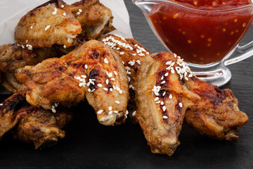 Baked chicken wings with sesame seeds and sweet chili sauce on dark background