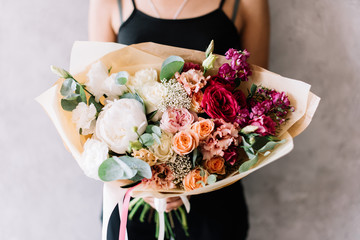 Very nice young woman holding beautiful blossoming flower bouquet of fresh peony, roses, carnations, eustoma, eucalyptus, chrysanthemum in gradient colours from white to red on the grey background