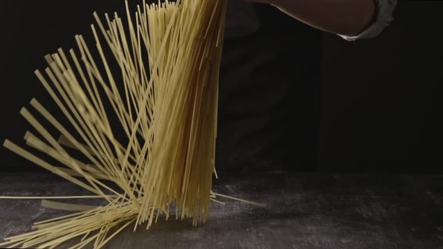 Cook's hand throws raw uncooked italian pasta on a wooden rustic table on a black background. Slow motion, Full HD video, 240fps, 1080p.