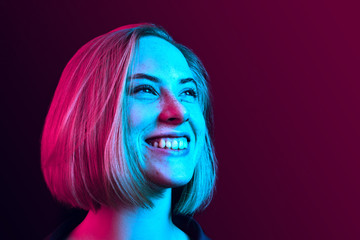 Happy business woman standing and smiling on neon studio background. Beautiful female half-length portrait. Young emotional woman. The human emotions, facial expression concept - obrazy, fototapety, plakaty
