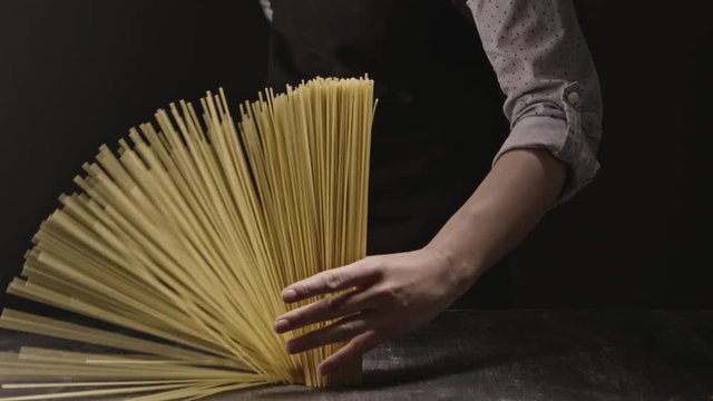 Woman's hand holds a bunch of italian pasta on a dark background. Slow motion, Full HD video, 240fps, 1080p.